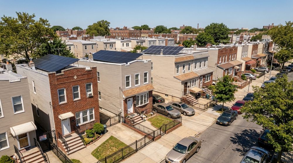 Attached row houses on a Queens, New York street with solar panels on the low-pitched roofs